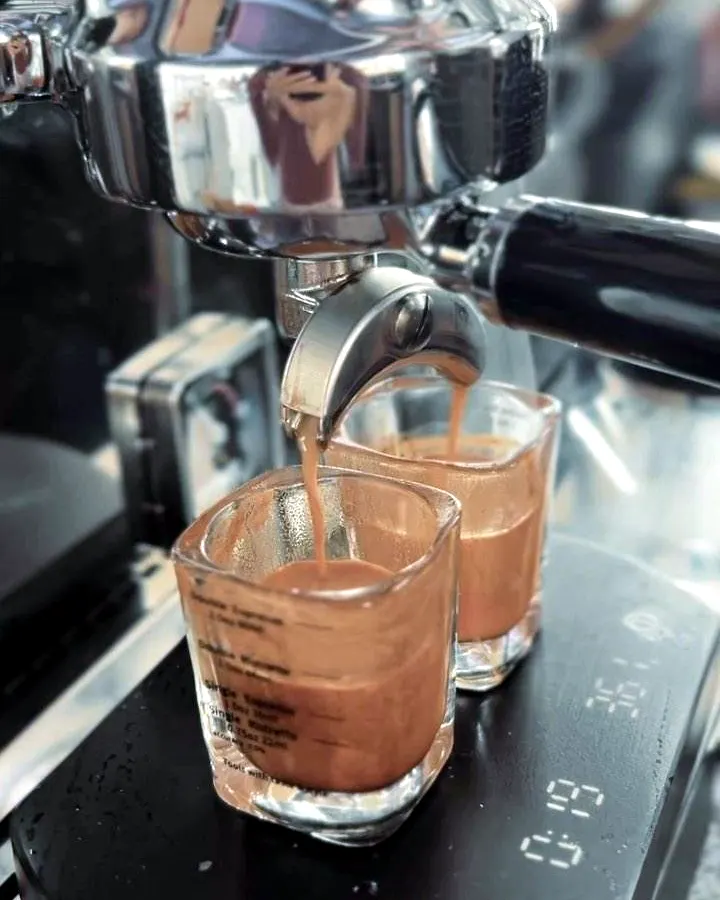 Espresso mengalir dari mesin kopi ke dua gelas kecil di atas timbangan