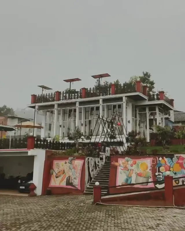 Bangunan DBon dengan payung di rooftop diselimuti kabut, dinding mural warna-warni di bawahnya
