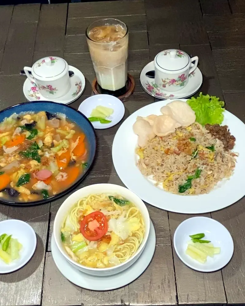 Aneka sajian DBon di meja kayu: cap cay, nasi goreng, sup, kerupuk, teh, dan minuman susu